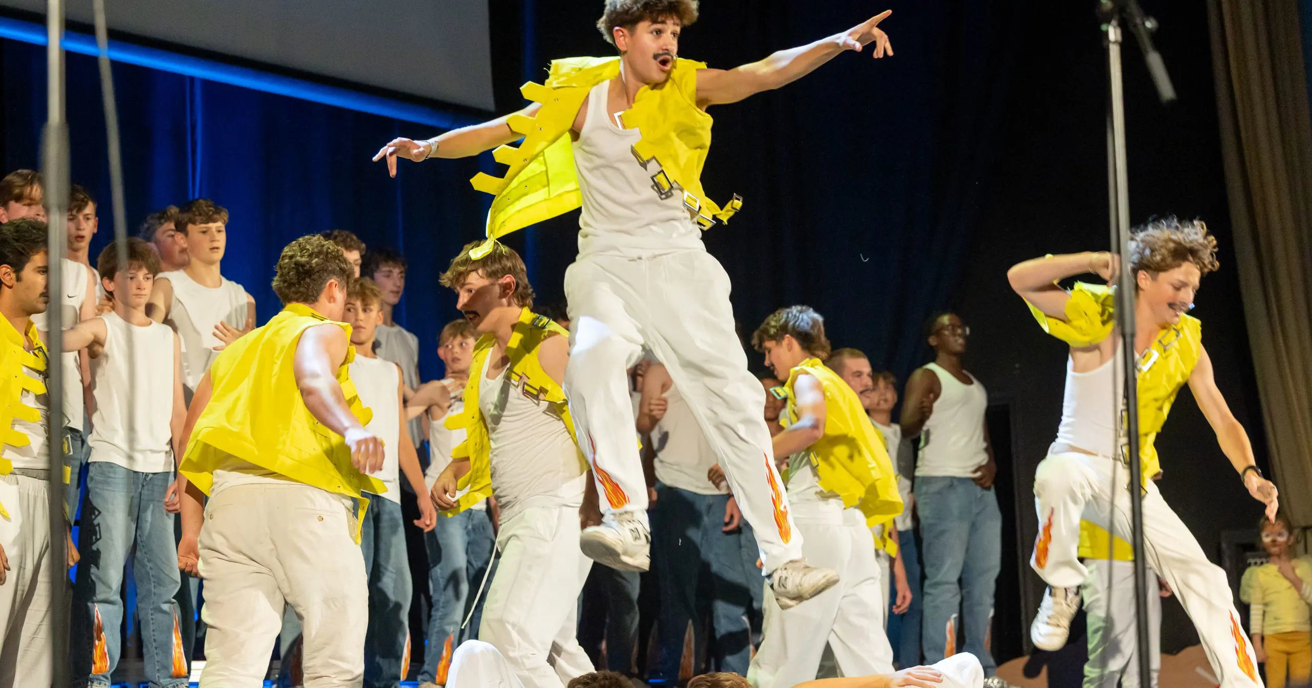 Boys singing in yellow jackets, one is jumping
