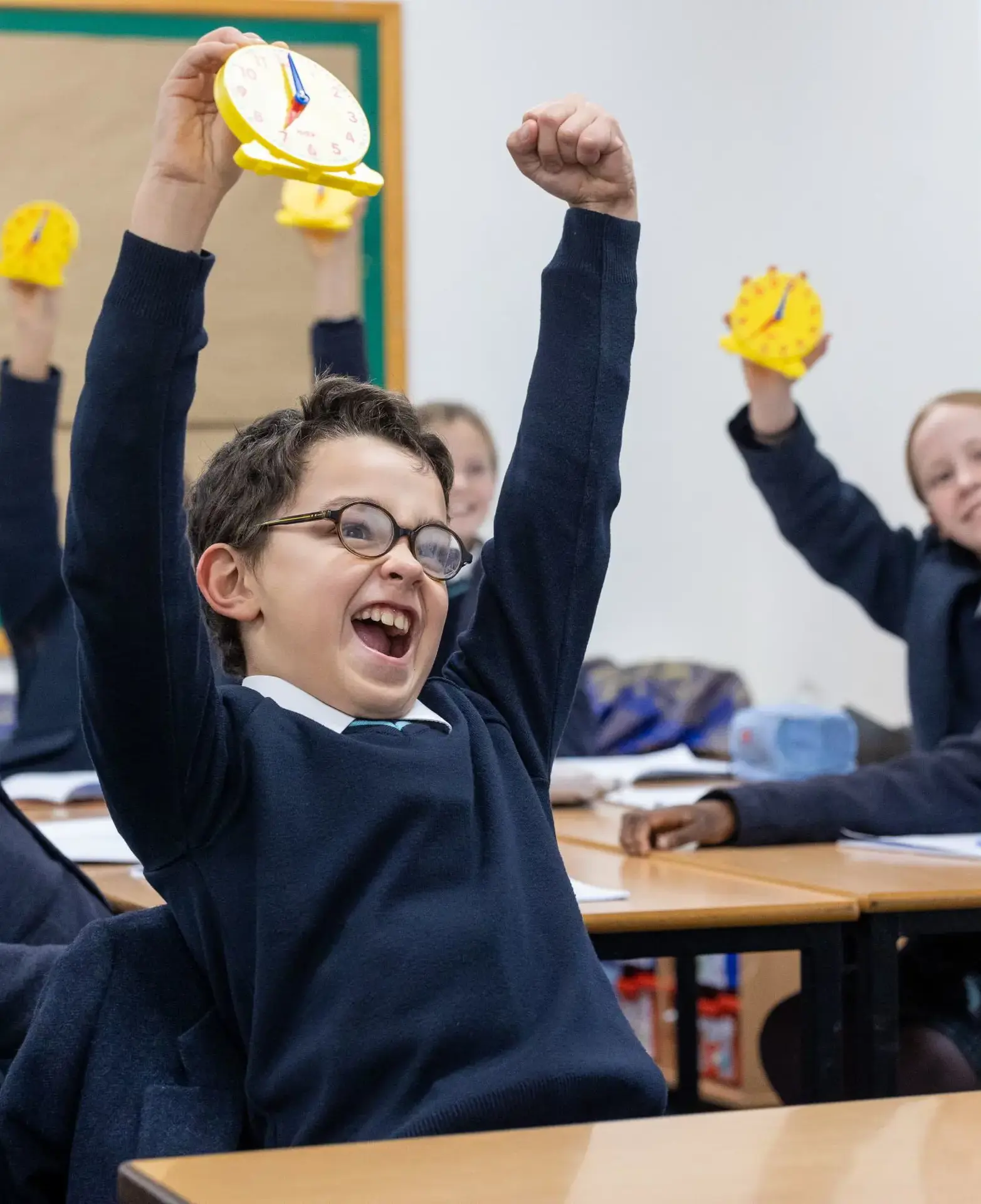 Classroom of happy pupils holding up their work