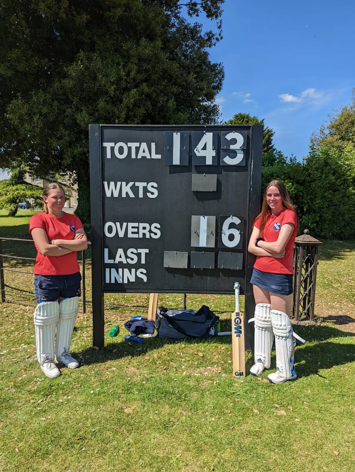 Students standing by cricket scoreboard at the end of a match.